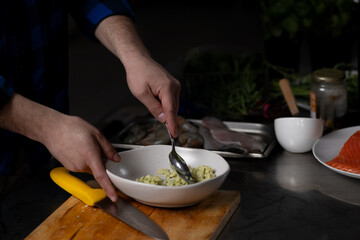Person mixing fresh ingredients in bowl. Kitchen setting includes various food items and utensils, indicating active meal preparation