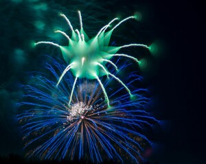 Fototapeta premium Colorful fireworks display lighting up the night sky with vibrant green and blue bursts.