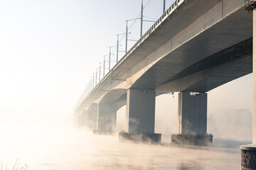 Bridge seen in dense fog over a river during a late winter morning. Winter landscape