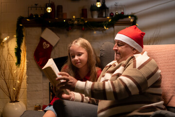 Grandfather and teenage girl are relaxing in the living room at home on Christmas night