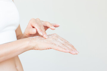 Fototapeta premium Young woman in white underwear gently applying a white sugar scrub on her hand to moisturize the skin. Body care
