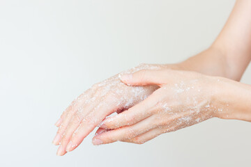 Close-up young woman in white underwear gently applying a white sugar scrub on her hand to...