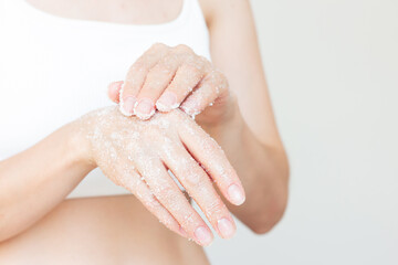 Fototapeta premium young Caucasian woman in white underwear applying a white sugar scrub to her hands to moisturize her skin. Body care. Close-up photo
