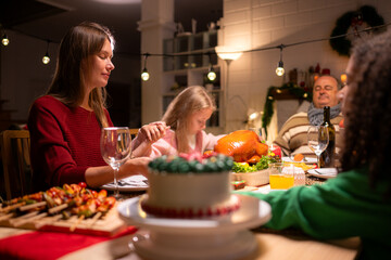 Grandfather, parents, and the teenage girls are all having dinner together at home on Christmas night