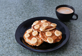 Desayuno de panqueques con banano y una taza de café.