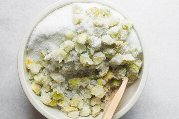 Overhead view of lime slices and sugar being mixed together in a white bowl, process of making lime cheong or lime syrup