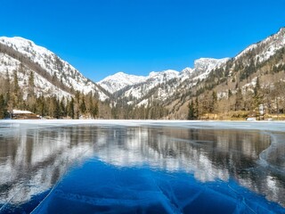 Frozen lake reflecting snow capped mountains under blue sky