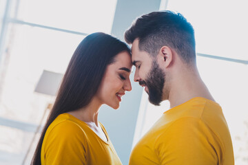Fototapeta premium Profile photo of two young partners closed eyes touch heads free time modern interior apartment indoors