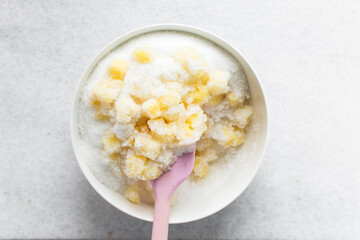 Overhead view of diced pineapple and sugar being mixed together in a white bowl, process of making...