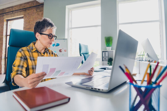 Photo of pretty senior female working graph papers wear plaid yellow shirt coworking successful nice light office - Powered by Adobe
