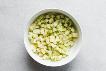 Top view of diced green apples in a white bowl, overhead view of chopped apples on a white background