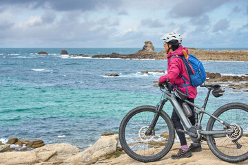 Fototapeta premium active senior woman cycling with her electric mountain bike at the rocky red granite cost next to Ploumanac'h, Côtes d'Armor,Brittany, France