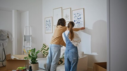 Married couple hanging artwork on wall new home. Spouses decorating living room