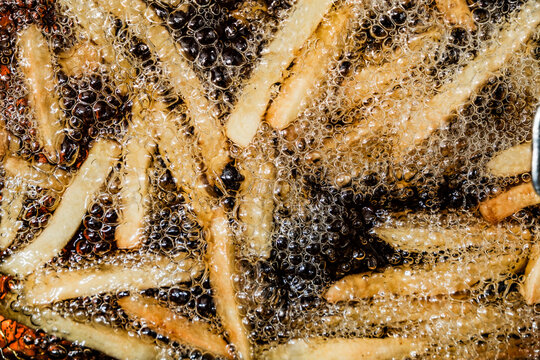 French fries bubbling in hot oil, captured up close as they cook to a crispy texture. The oil bubbles around the fries, creating a mesmerizing pattern of light and texture.