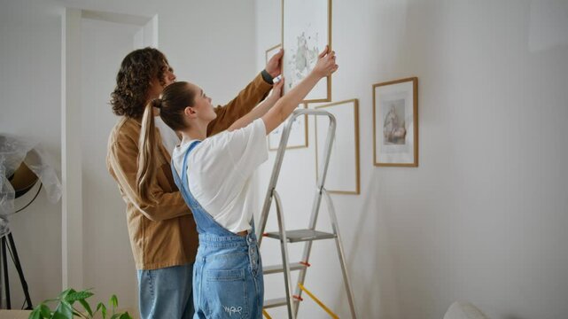 Family discussing home decoration holding framed artwork in light living room. 