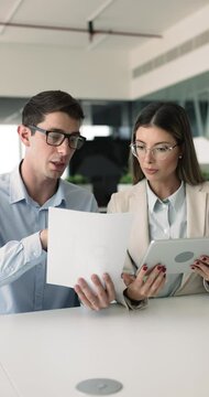 Two European colleagues working together using tablet hold papers, review documents, discuss business-related matters or information relevant to their joint task. Teamwork, professional interaction