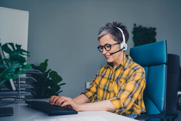 Photo of nice retired woman headset support manager wear plaid shirt comfortable modern office loft room interior indoors workspace