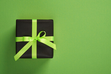 Horizontal banner with one black gift box with neon green ribbons. Green background, space for your...