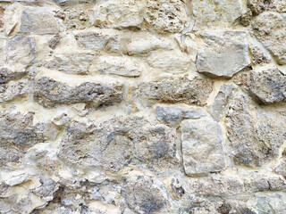 Textured stone wall with a rustic appearance, showcasing natural color variations and weathering, likely from an historical structure