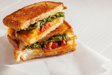 Delicious gourmet homemade sandwich with fried egg and melted cheese, tomato slices and basil leaves
