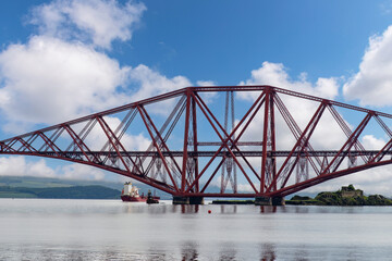Obraz premium Ship sailing under the red Forth cantilever railway bridge across the Firth of Forth, Queensferry, UK near Edinburgh