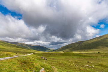 Fototapeta premium Panoramic view over the green Northwest Highlands of Scotland near Glen Moriston, Inverness, UK with cloudscape of large cumulus clouds in blue sky