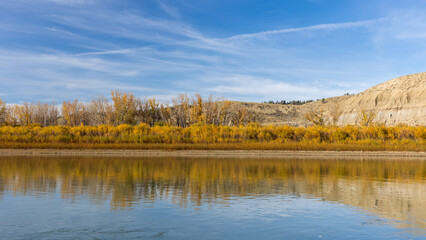 In Phillips County, Montana, autumn paints the riverbanks with vivid fall foliage, where colorful leaves reflect in calm waters under crisp skies.