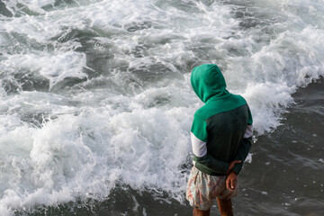 Man with a hood standing on a pier and looking at the Atlantic Ocean. Shorts, sandals. Casablanca, Morocco.