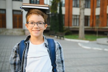 Back to school. Pupil of primary school on the way to study. Little first grader in glasses and with school bag. Beginning of lessons. First day of fall. Boy outdoors near school building