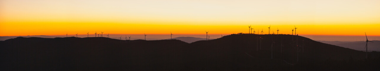 Obraz premium a landscape of wind turbines silhouetted against a vibrant sunset.