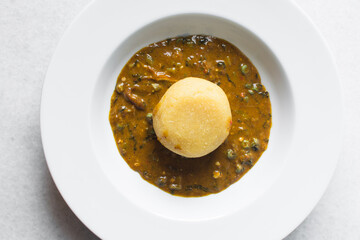 Overhead view of nigerian ogbono soup and eba on a white plate, top view of ogbono draw soup with garri in a soup plate, flatlay of nigerian ogbono and okra soup