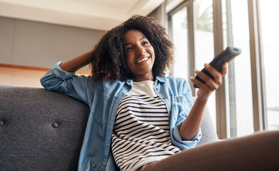 Happy, black woman and watching tv with remote on sofa for entertainment, movie or series at home....