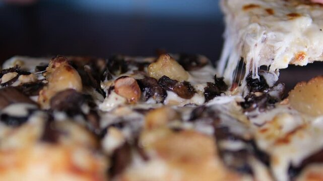 girl in blue sweater preparing to eat pizza with mushrooms on a wooden board Cook takes a slice of bacon, mushroom and cheese pizza. Hand in rubber glove close-up
