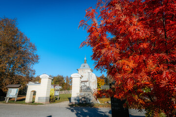 A historic structure with a weathered dome stands beneath a clear blue sky, framed by vibrant red...