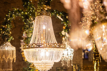 An elegant chandelier adorned with crystals and greenery, illuminating a festive setting during the holiday season. Background with Luxurious Christmas decorations and crystal chandeliers and lights