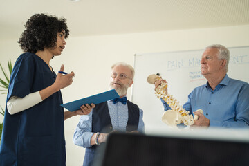Diverse medical team discussing pain management, spine anatomy demonstration, healthcare education seminar
