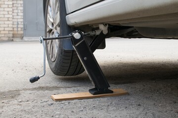 The front wheel of the car is jacked up for replacement. A board is placed under the jack