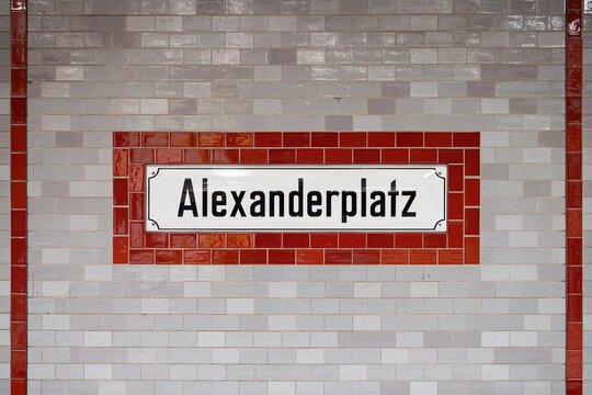 Alexanderplatz sign at the underground train station in Berlin Mitte, Germany. Location name of the public transportation. Red and gray tiled wall with black letters on white.