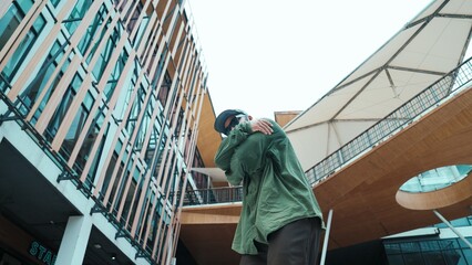 Low angle view of hipster pose in hip hop style surrounded by mall view. Portrait of sporty asian hip hop choreographer dancing break dance while looking at camera. Outdoor sport 2024. Hiphop.