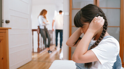 Obraz premium Stressed and unhappy young girl huddle in corner, cover her ears blocking sound of her parent arguing in background. Domestic violence at home and traumatic childhood develop to depression. Synchronos