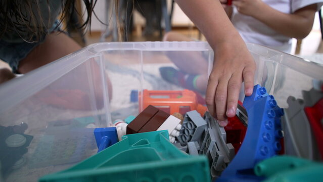 Close-up of a child’s hand picking toy building blocks from a plastic container, organizing colorful toy pieces on the floor for creative play in a home environment