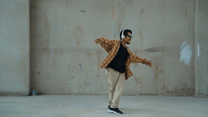 Attractive hispanic dancer in casual look practice street dance while listen music from headphone at cement background. Motion shot of break dancing performance. Outdoor sport 2024. Hiphop. © InfiniteFlow