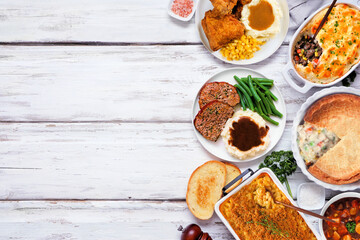 Cozy comfort food side border. Overhead view over a white wood background. Meatloaf, stew, pot pie, mac and cheese, grilled cheese, soup, fried chicken, shepherds pie and warm sides. Copy space.