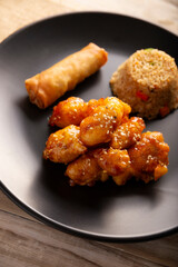 Sweet and sour chicken with fried rice and crispy spring roll, American Chinese food made out of fried, battered chicken covered with sauce. Tasty dish popular in many countries.