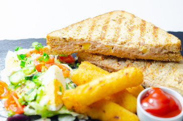 A plate of food with a sandwich, cheese sticks, and ketchup