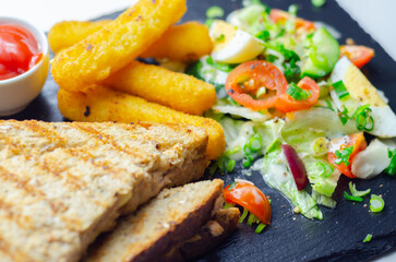 A plate of food with a sandwich, cheese sticks, and ketchup