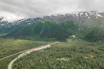 Aerial panoramic view of traveling cars and Alaska Railroad Train waiting to cross Anton Anderson Memorial Tunnel to Whittier, Alaska with surrounding mountain and glacier landscape