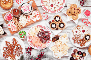 Christmas holiday cookies and desserts table scene. Overhead view on a white wood background. Cookies, tarts, chocolates and hot chocolate tray.