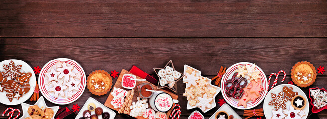 Christmas holiday cookies and desserts bottom border. Top view on a dark wood banner background. Cookies, tarts, chocolates and hot chocolate tray.