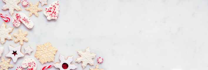 Christmas baking corner border with a variety of red and white theme cookies and candies. Above view on a white marble banner background with copy space. Holiday candy cane baking concept.